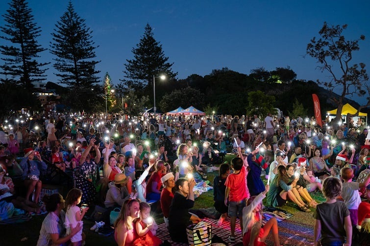 Crowds gathered on picnic blankets under the evening sky at North Burleigh for one of the most-loved Christmas events Gold Coast locals attend, with people holding up phone lights during the carols by the sea celebration.